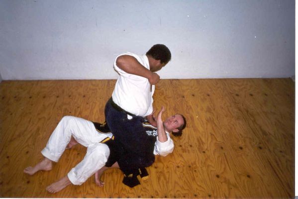 A01- Master Wachsmann is mounted by Chief Instructor King, who is preparing to bring down some punches. Master Wachsmann uses his heels to push off the floor, scooting his body up and moving the opponent down onto his hips